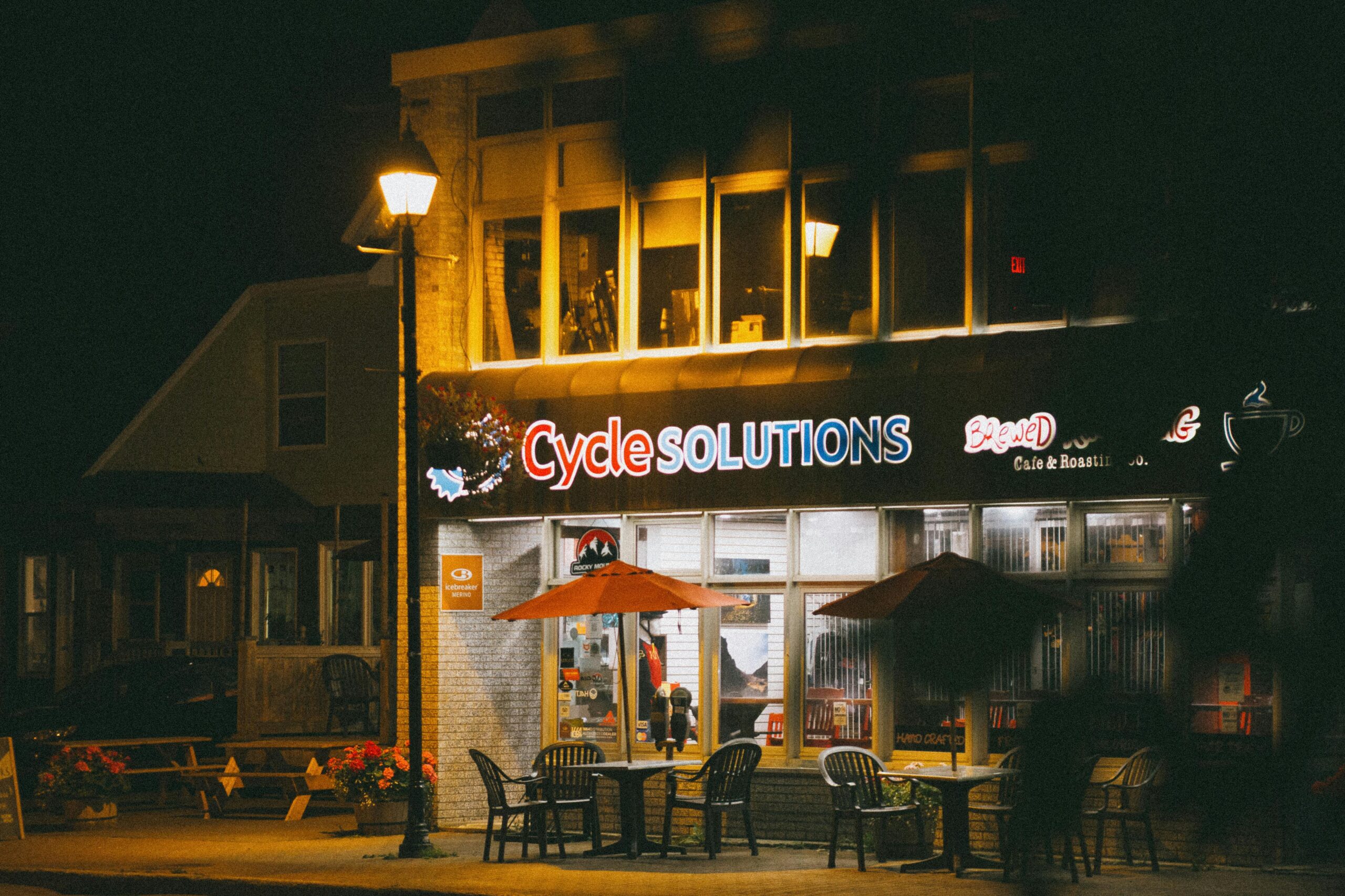 Nighttime view of Cycle Solutions café, a cozy spot for relaxation with warm lighting and outdoor seating.